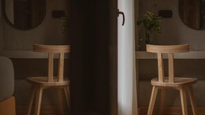 A room with two wooden chairs, a white pillar, and a mirror on the wall.