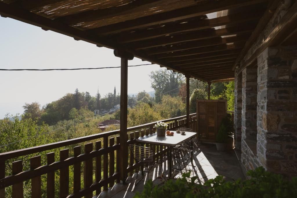 A covered outdoor seating area with a table and chairs, a stone wall, and a view of the landscape.