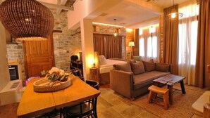 A cozy living room with a wooden dining table, a sofa, and a coffee table. There is a stone wall and a wooden door in the background.