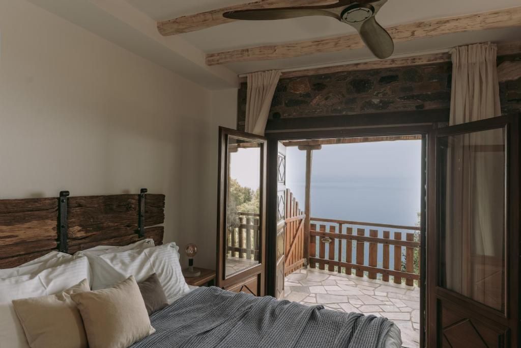 Un dormitorio con cabecera de madera, cama con almohadas, ventana con cortinas y vista al mar.