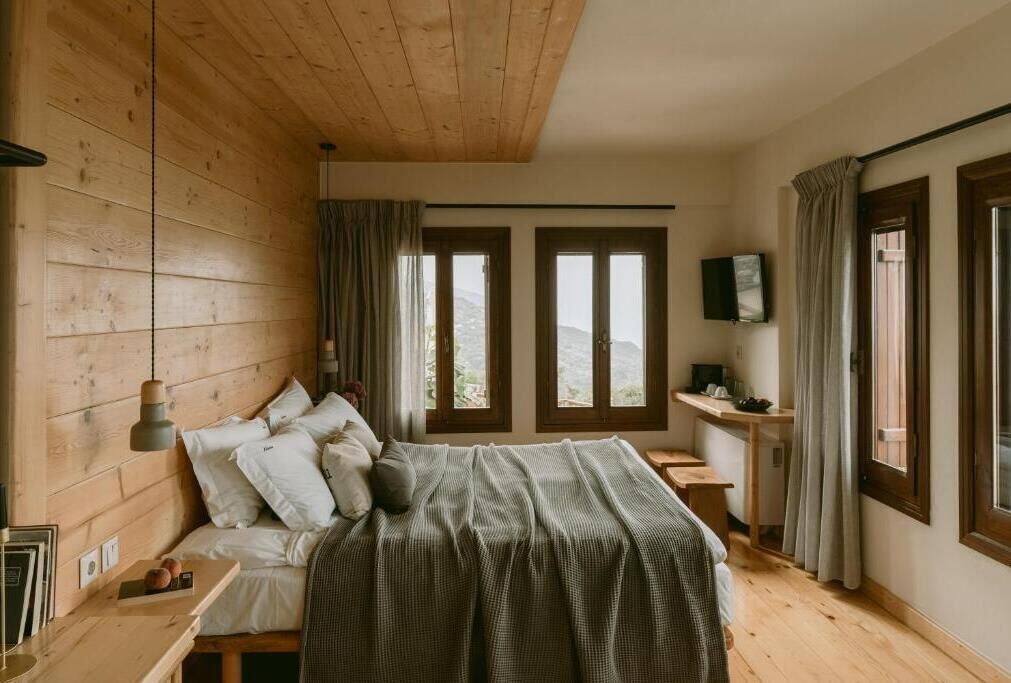 Une chambre avec un plafond en bois, un lit recouvert d’une couverture à rayures, deux fenêtres, une table de chevet et un téléviseur fixé au mur.