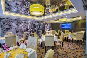 Un espace repas avec des tables dressées pour le service, un écran de télévision et une moquette à motifs.