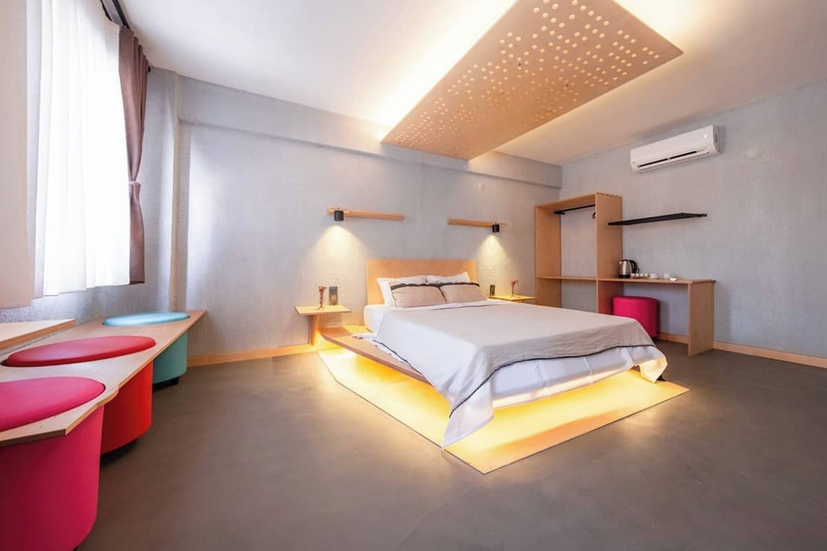 Ein modernes Hotelzimmer mit Bett, Nachttischen, Schreibtisch, Stuhl, Spiegel und Klimaanlage.