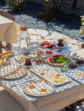 A table set outdoors with various dishes, including a plate of eggs, a glass of water, and a bottle of water. - Bi Salkım Perla Otel (Bozcaada)