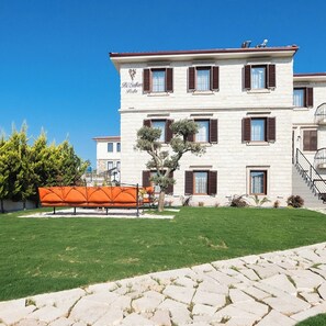 A multi-story building with a white facade and brown shutters, a stone pathway, and a well-maintained lawn. - Bi Salkım Perla Otel (Bozcaada)