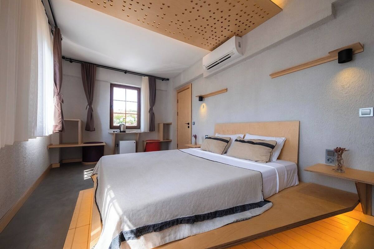 Ein modernes Hotelzimmer mit einem großen Bett, eingebauten Regalen, einem Schreibtisch und einem Fenster mit Vorhängen.
