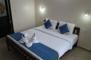 A neatly made bed with white linens and blue accents, a wooden headboard, and a wall-mounted light fixture. - My Sea Side Budget Stay (Calangute)