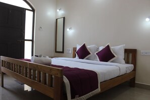A bedroom with a wooden bed, white bedding, and purple pillows. - My Sea Side Budget Stay (Calangute)