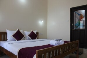 A neatly made bed with a wooden headboard, a dark door with a glass panel, and a small bedside table with a remote control. - My Sea Side Budget Stay (Calangute)