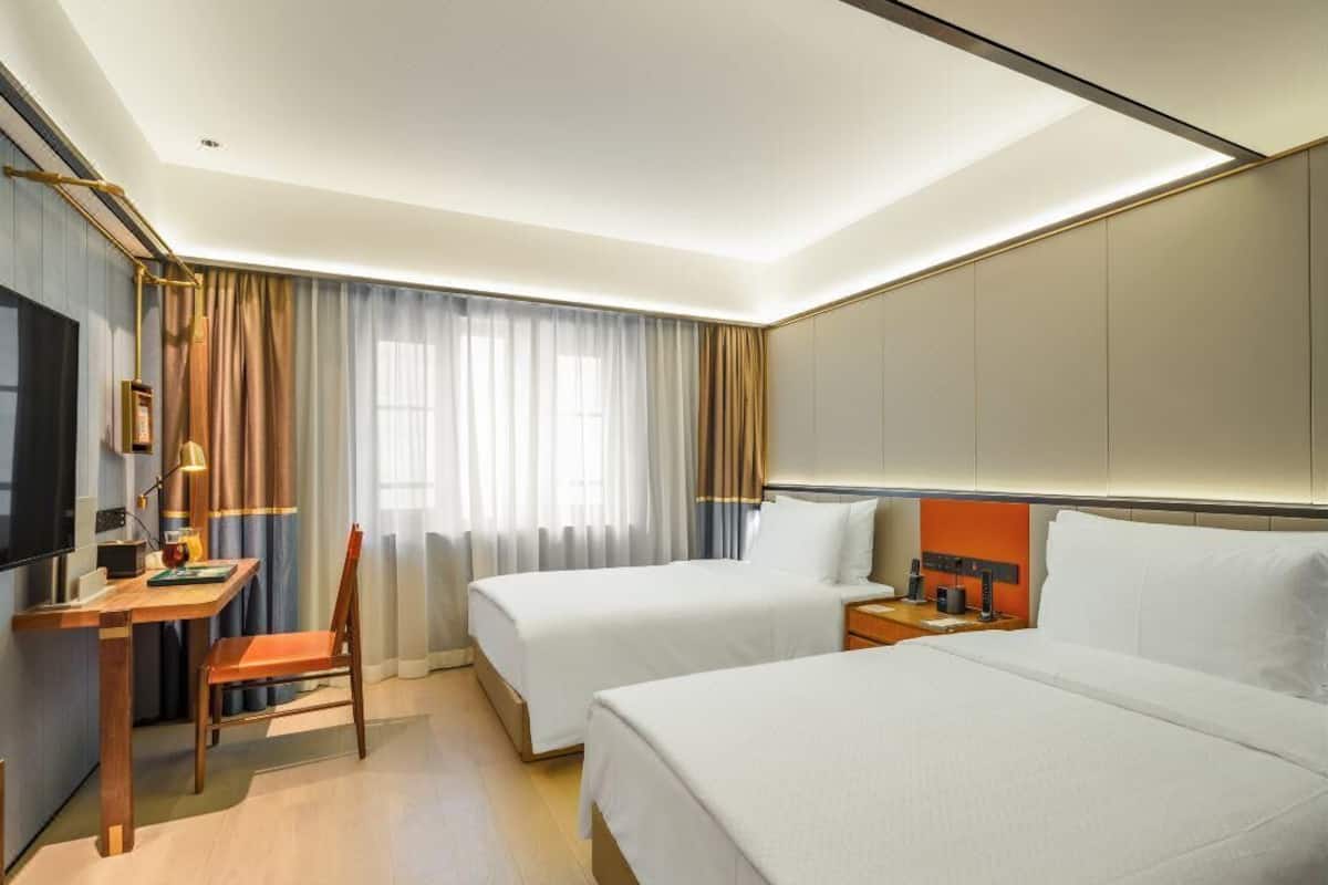 Habitación de hotel con dos camas, un escritorio, una silla, un televisor y una ventana con cortinas.