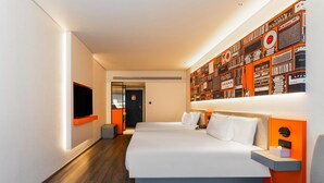 Moderni hotellihuone, jossa on suuri sänky, taulutelevisio, seinälle asennettu taideteos ja pieni oleskelualue.