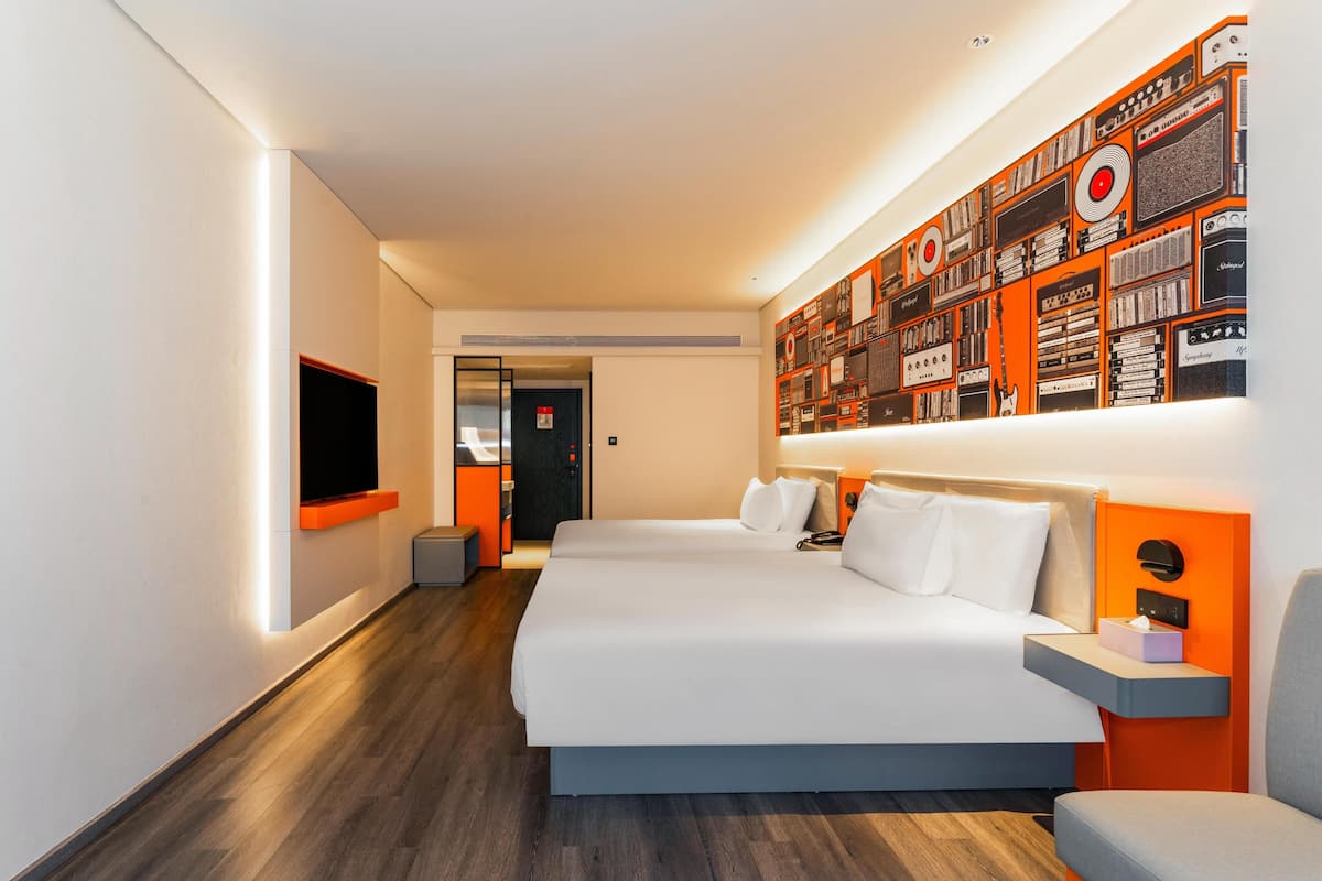 A modern hotel room with a large bed, a flat-screen TV, a wall-mounted artwork, and a small seating area.