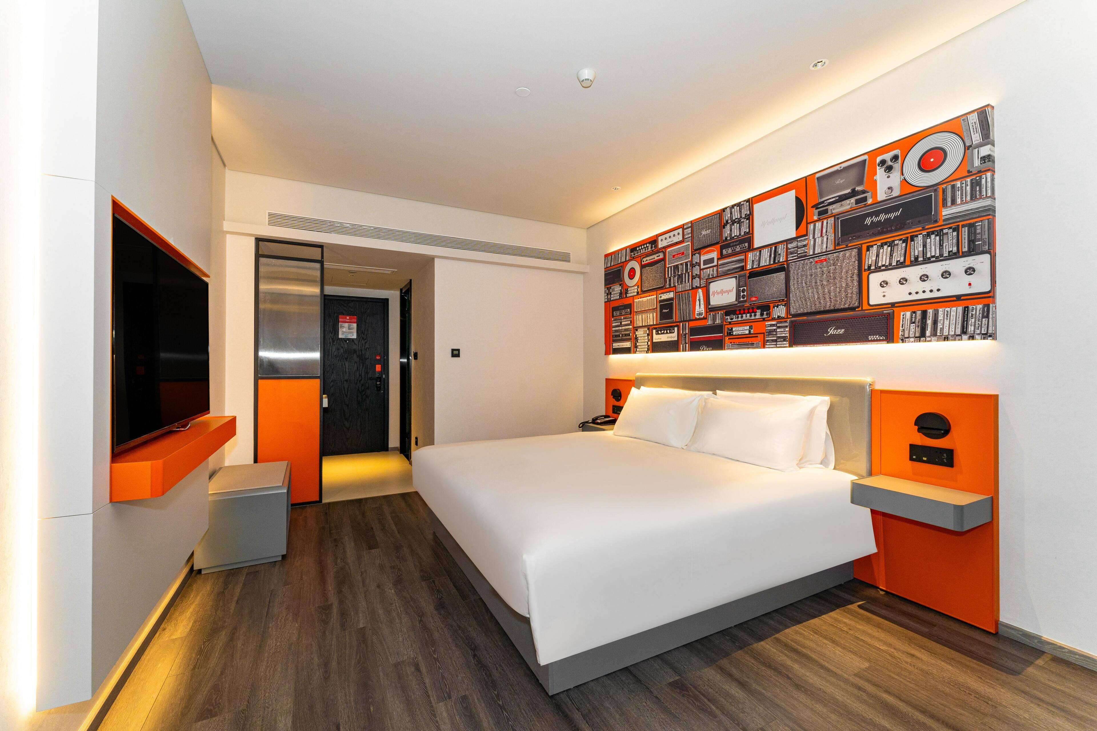Ein modernes Hotelzimmer mit einem großen Bett, einem Flachbildfernseher, einer wandmontierten Musikanlage und einer Tür zum Badezimmer.