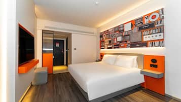 A modern hotel room with a large bed, a flat-screen TV, a wall-mounted sound system, and a door leading to the bathroom.