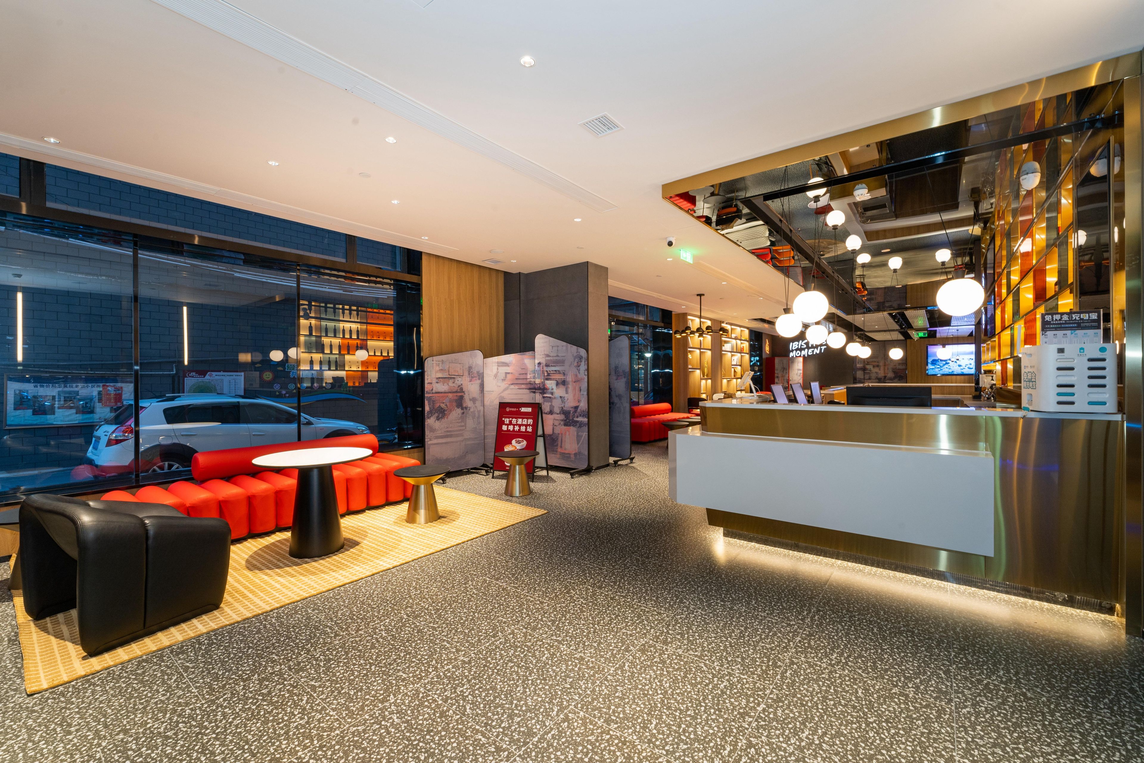 A modern hotel lobby with a reception desk, seating area, and large windows.