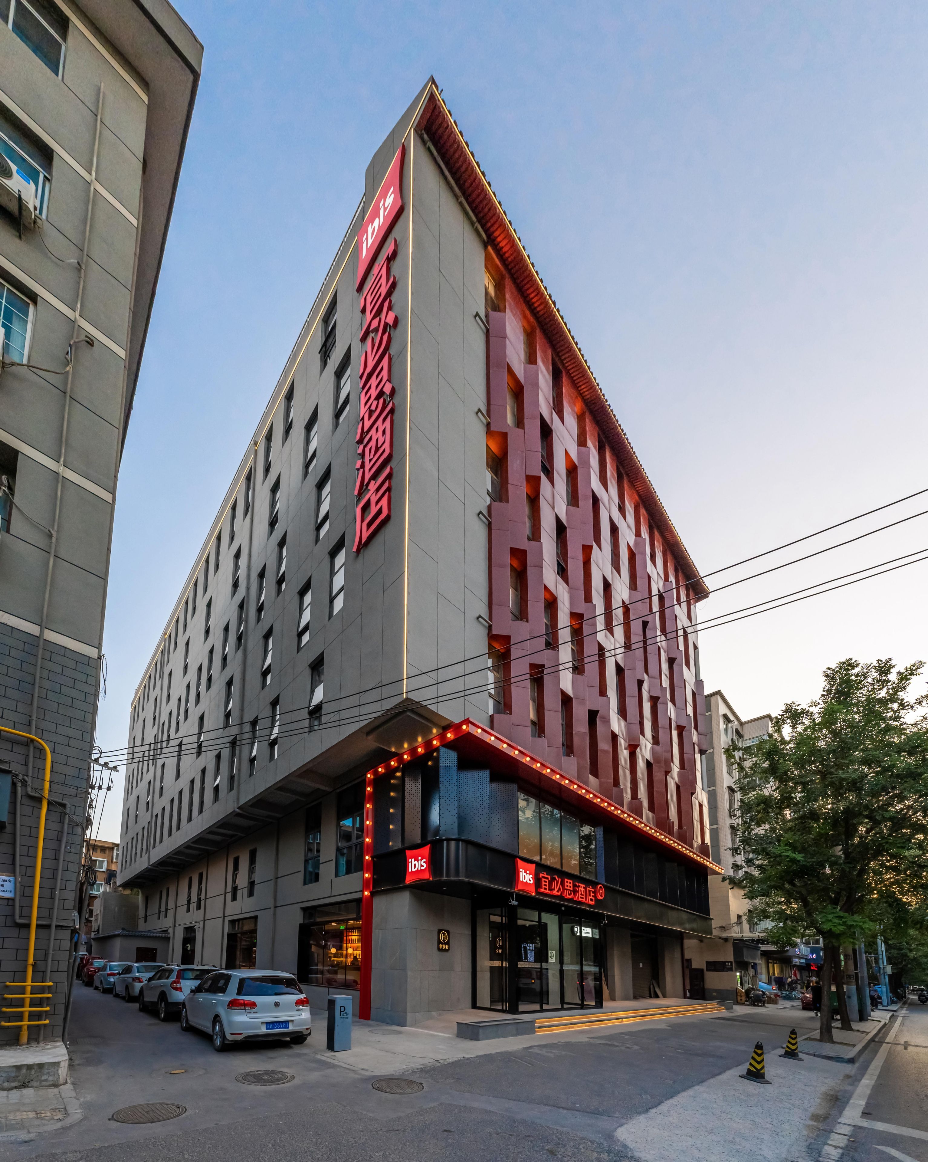 Un hotel moderno con una fachada destacada en rojo y gris, varios pisos y una entrada a nivel de calle con señalización iluminada.