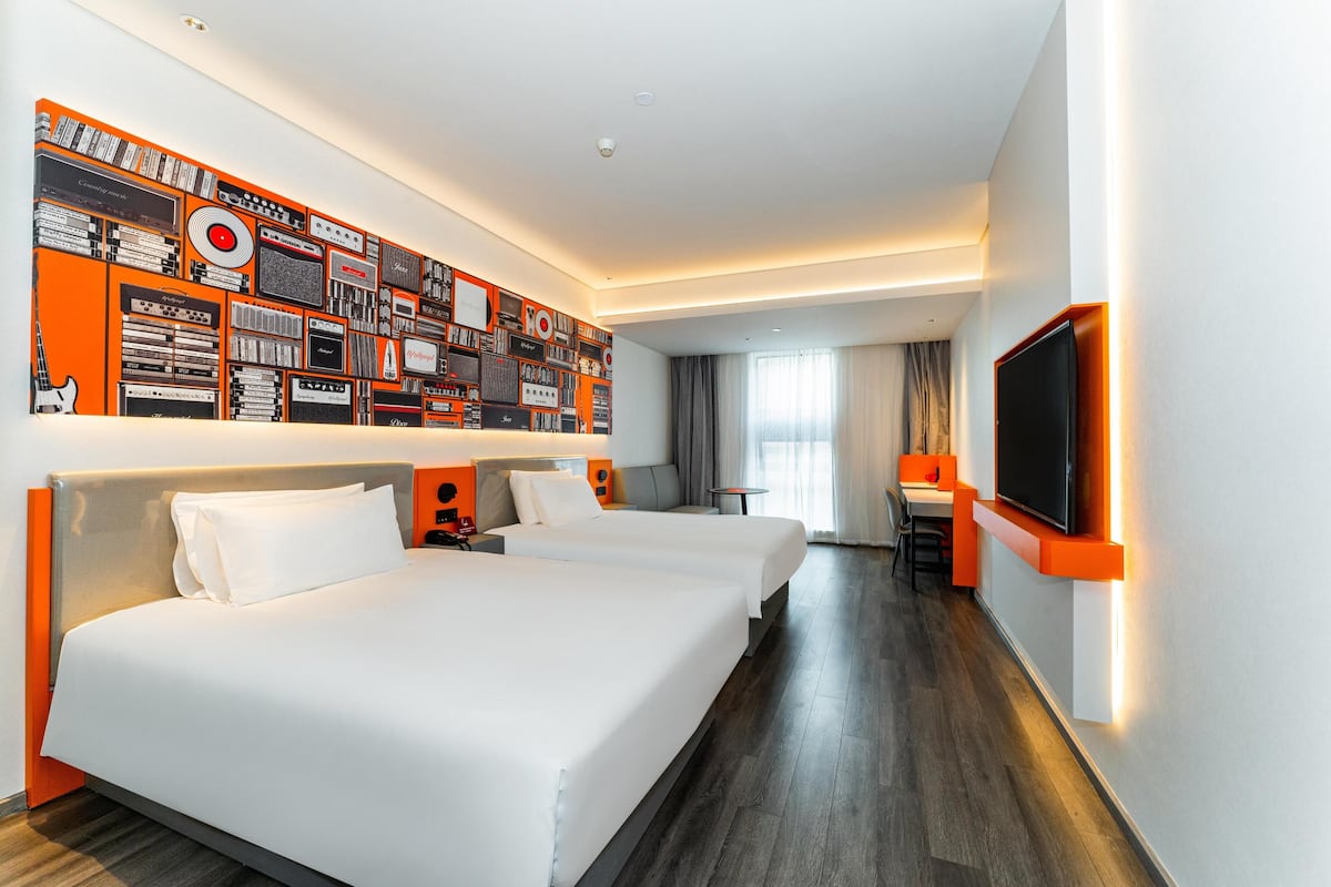 A hotel room with two beds, a TV, a desk, and a wall with various items.