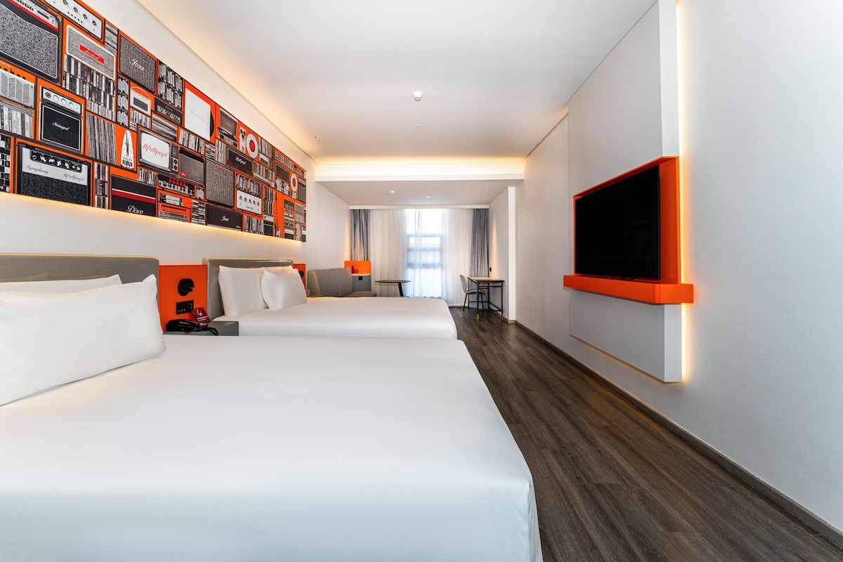 Habitació d'hotel amb dos llits, una televisió, una paret amb dissenys de ràdios antigues i vista al passadís.