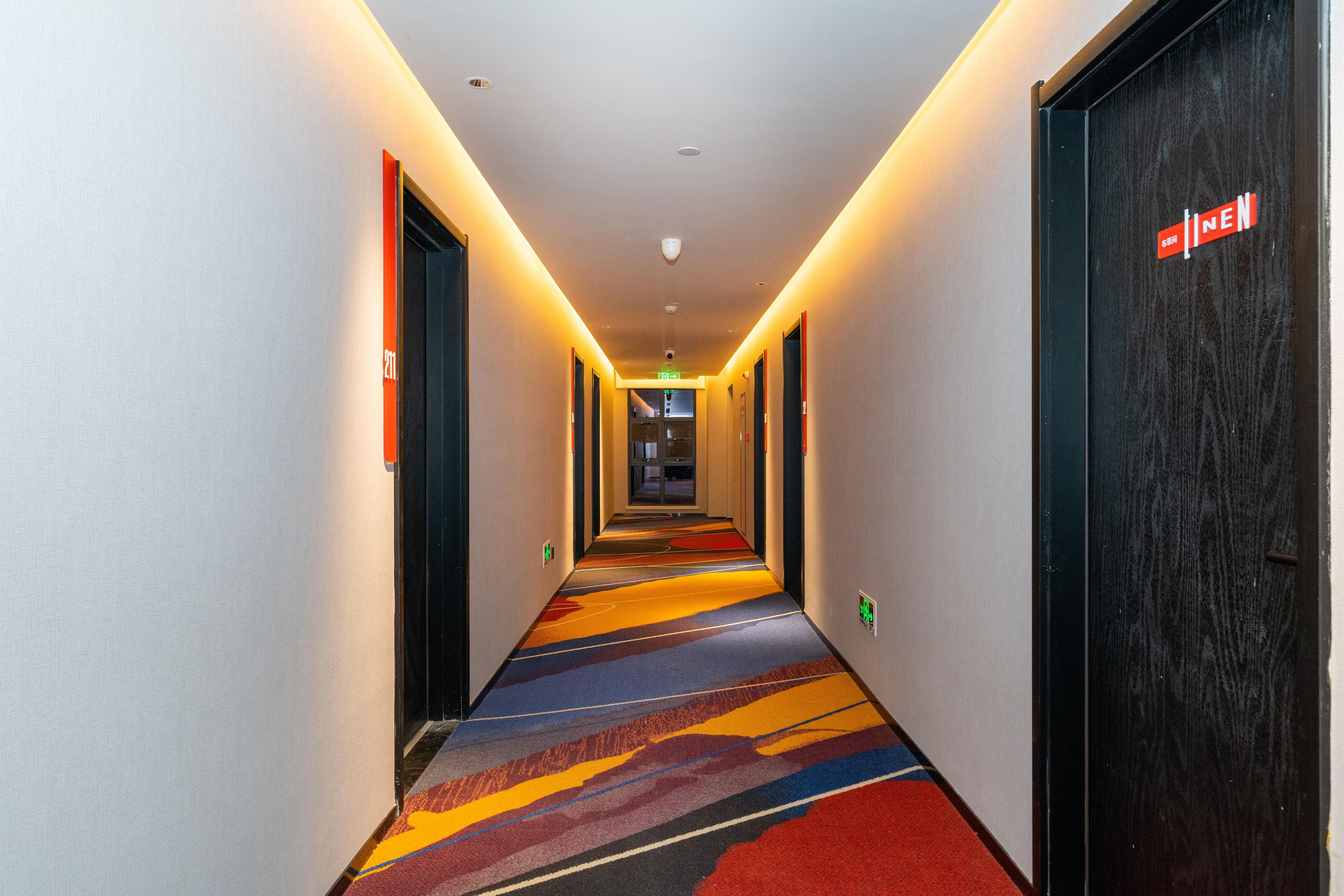 A hotel hallway with a carpeted floor, doors on both sides, and a sign on the right door.