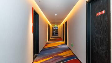 A hotel hallway with a carpeted floor, doors on both sides, and a sign on the right door.