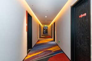 A hotel hallway with a carpeted floor, doors on both sides, and a sign on the right door. - Ibis Xian Bell Tower Huimin Street (Xi'an)