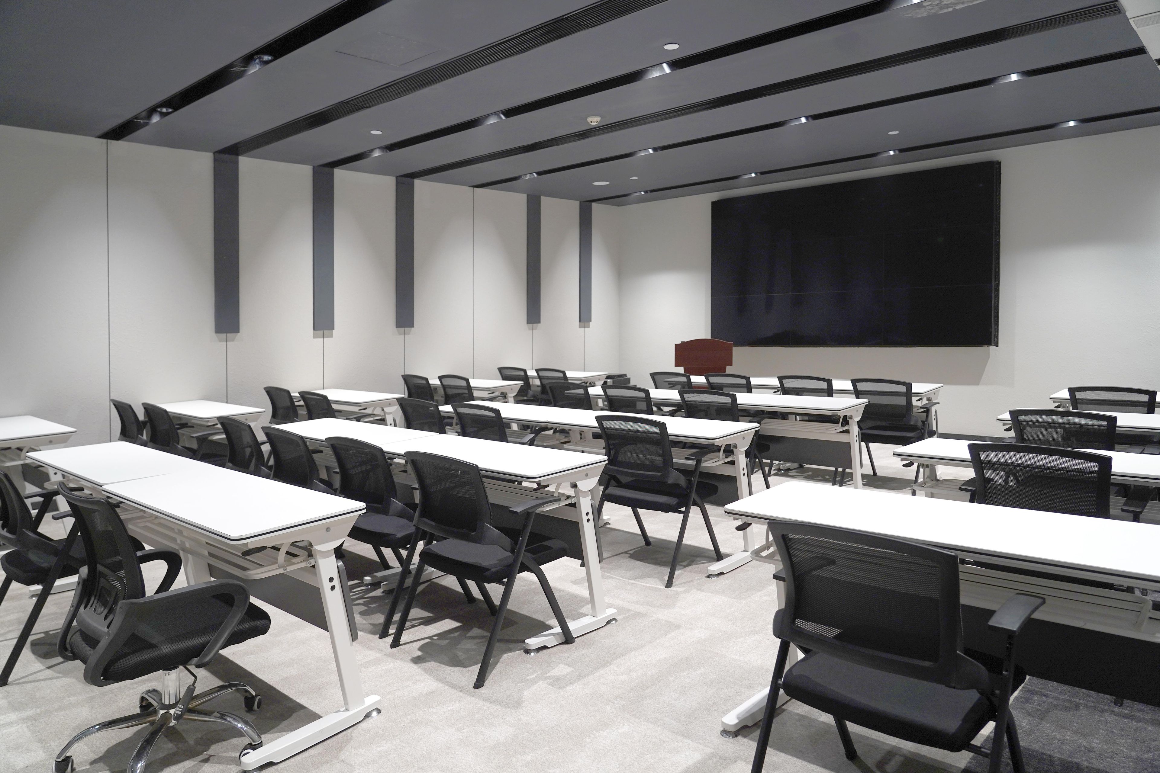 A conference room with multiple tables and chairs, a large screen, and a projector.