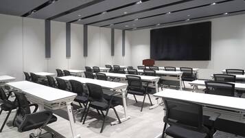 Un salón de conferencias con varias mesas y sillas, una pantalla grande y un proyector.
