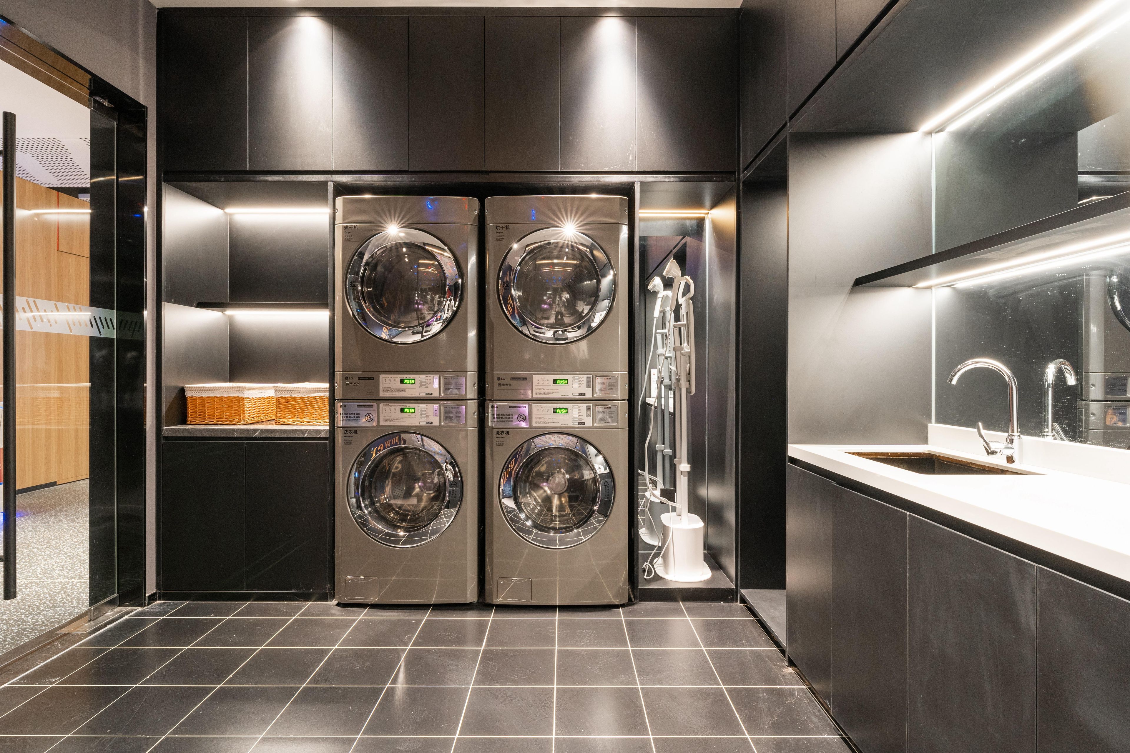 A modern laundry room with two stacked washing machines, a sink, and a mirror.
