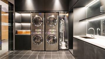 A modern laundry room with two stacked washing machines, a sink, and a mirror.