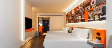 A modern hotel room with a large bed, a flat-screen TV, a wall-mounted artwork, and a small seating area.