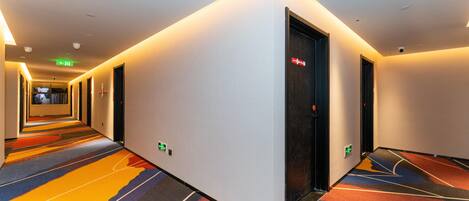 A hotel hallway with patterned carpet, a door with a sign, and an emergency exit sign.