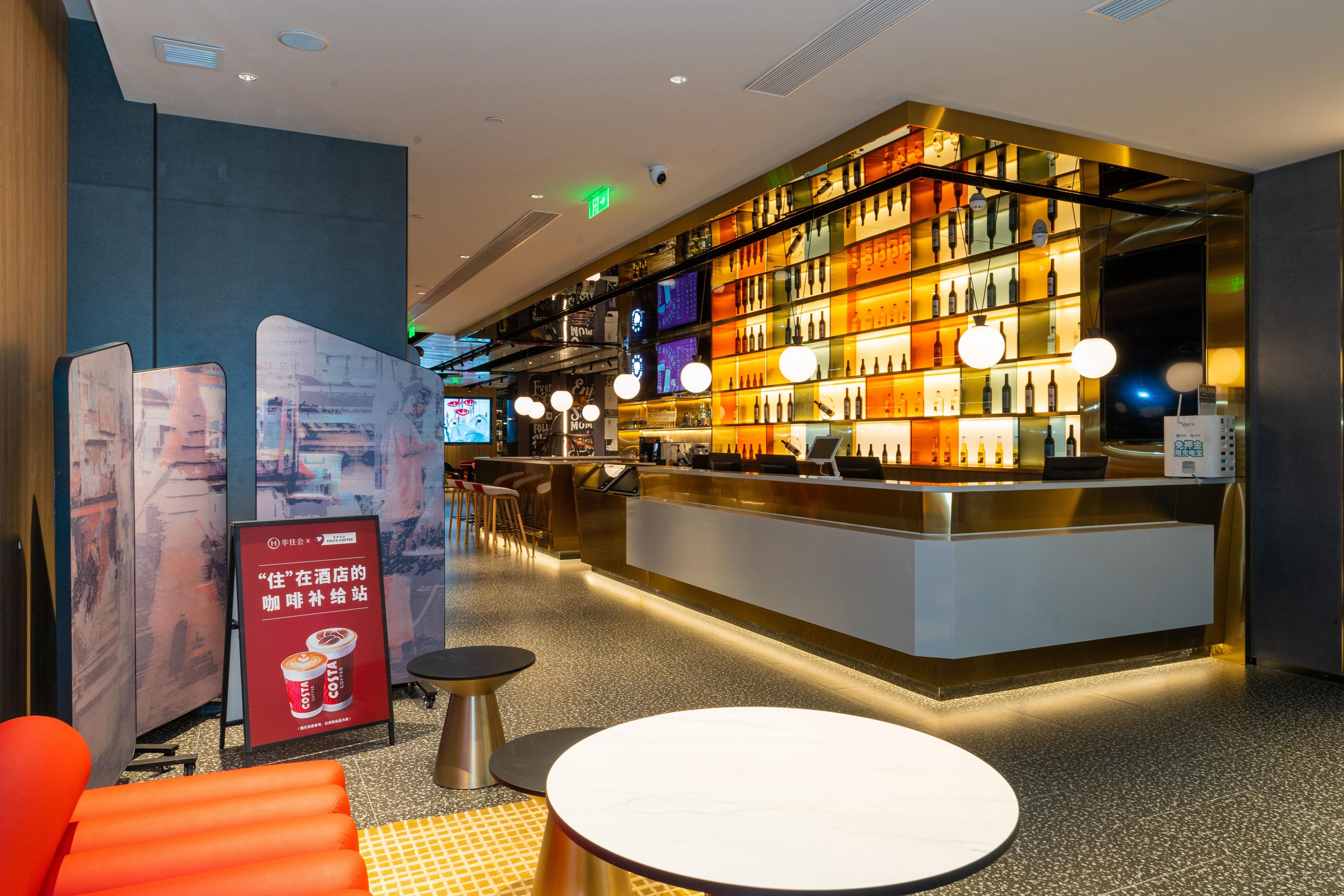 A modern hotel lobby with a bar area, seating, and a digital screen.