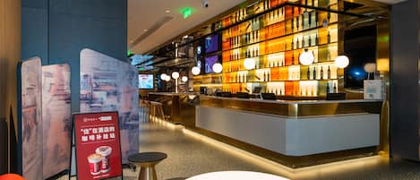 A modern hotel lobby with a bar area, seating, and a digital screen.