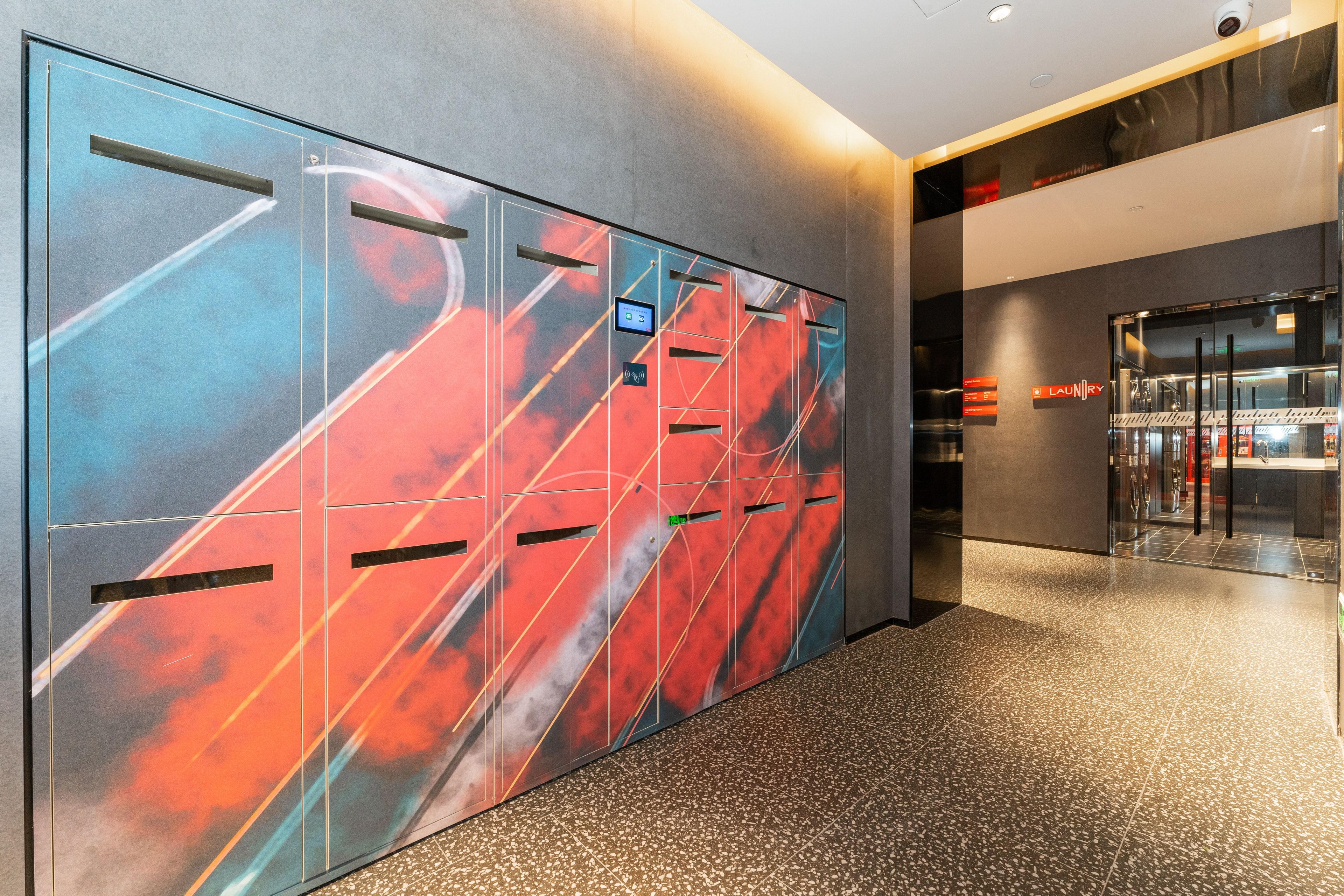 A modern hallway with lockers, a digital display, and a sign for a laundry facility.