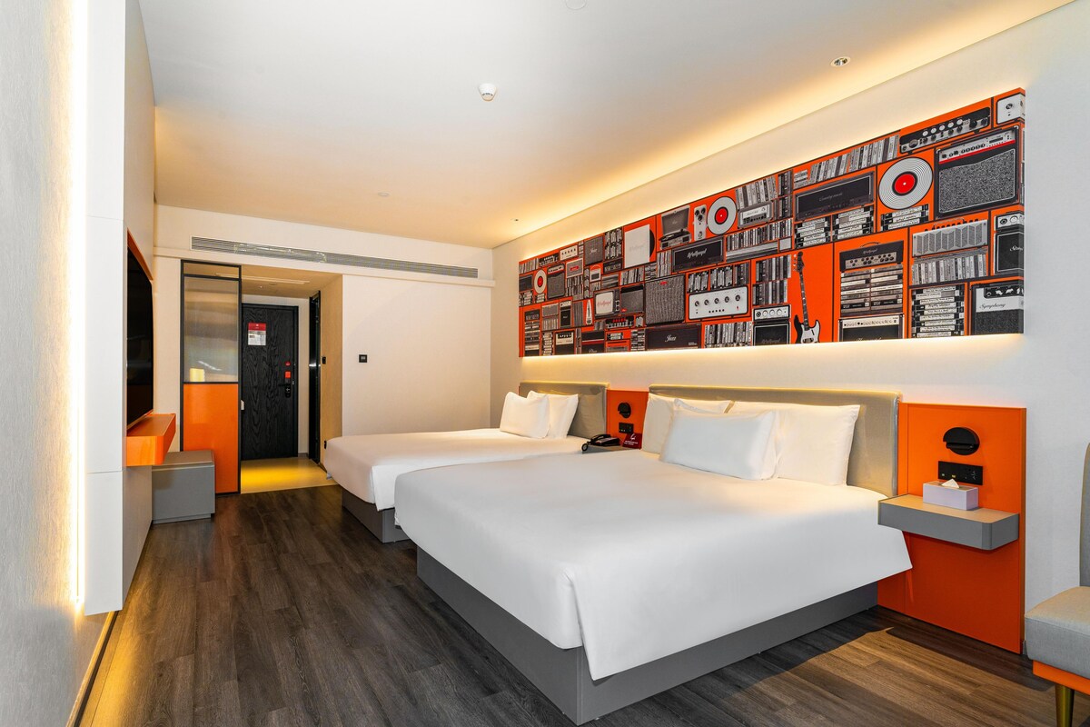 Habitació d'hotel amb dos llits, una paret amb diversos aparells de so, un escriptori petit i una cadira.