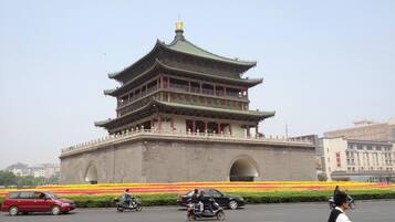 A multi-tiered traditional building with a green roof, surrounded by a flower bed with yellow and red flowers.