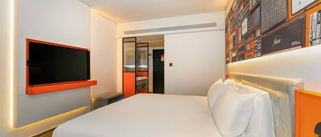 Una habitación de hotel moderna con una cama grande, un televisor de pantalla plana en la pared y una estantería con varios objetos.