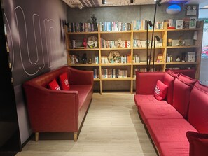 A modern interior with two red sofas, a bookshelf filled with books, and a wall with abstract art. - Ibis Hotel (Shanghai)