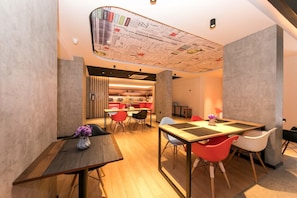 Un intérieur moderne avec un coin repas comprenant une table en bois et des chaises colorées, une cuisine en arrière-plan et un design de plafond original.