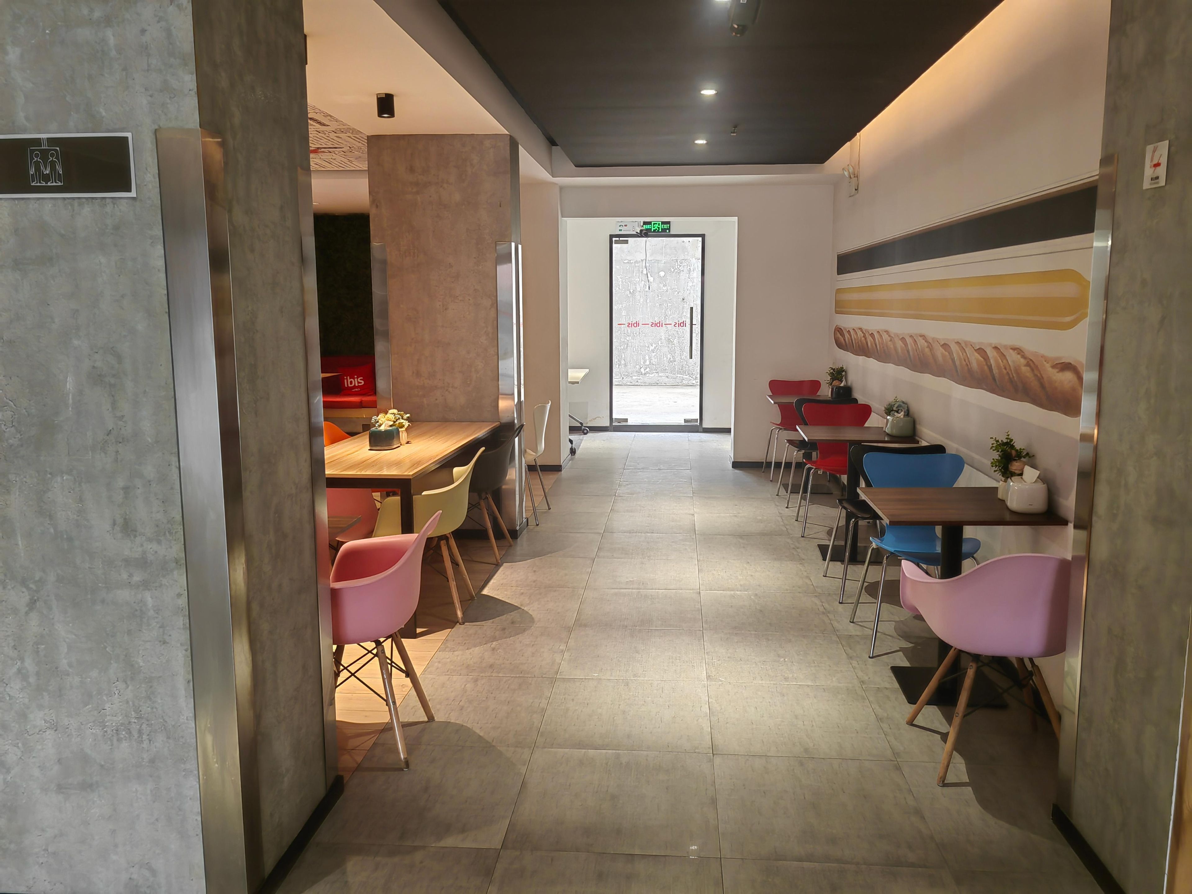 A modern interior with a long dining area, colorful chairs, and a large wall mural.