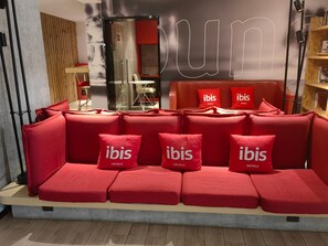 A red sofa with 'ibis HOTELS' branded pillows, a wooden wall, and a glass partition. - Ibis Hotel (Shanghai)