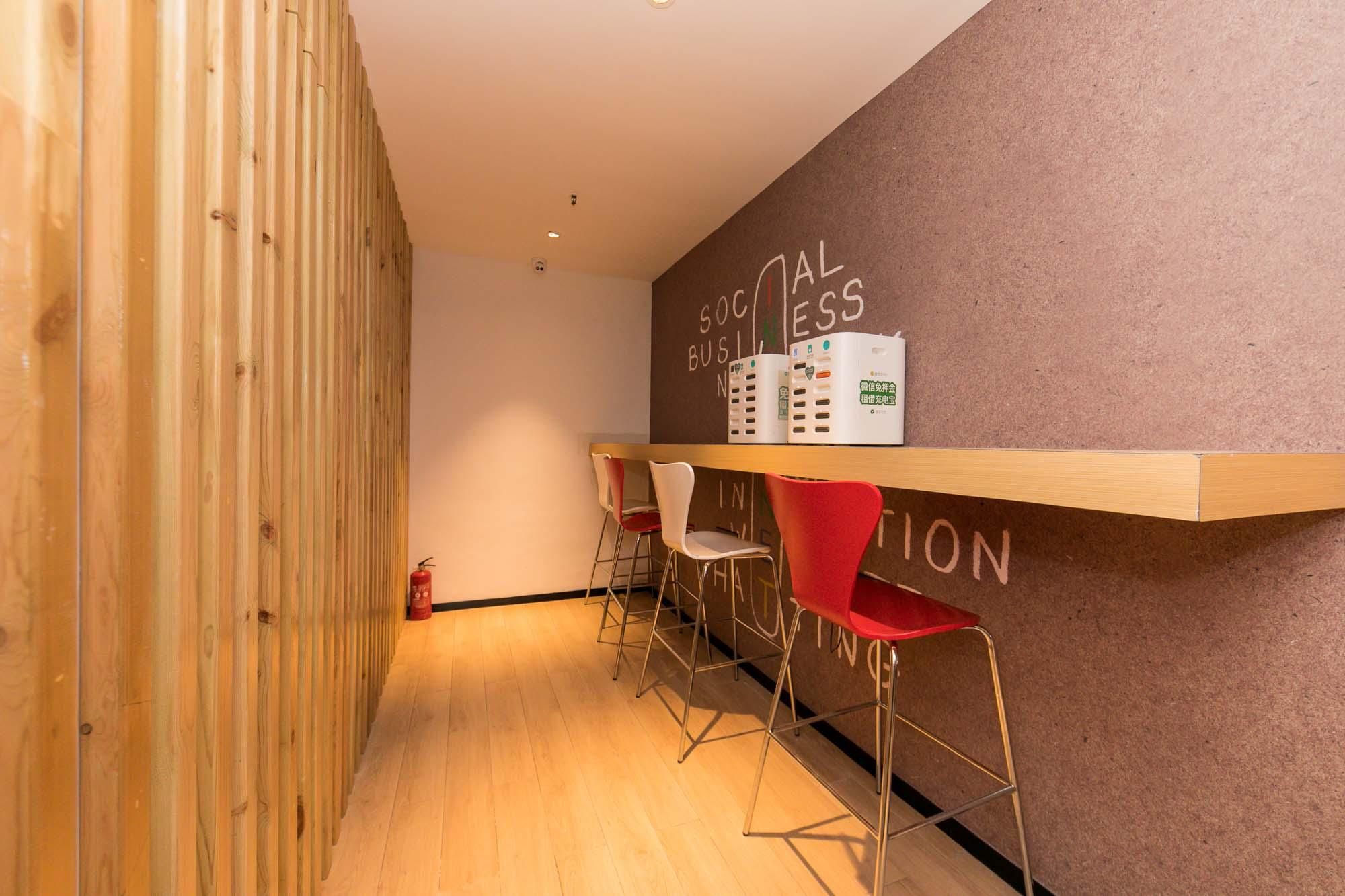 A reception area with a wooden wall, a bulletin board with text, and three red bar stools.