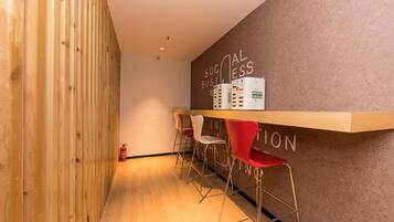 A reception area with a wooden wall, a bulletin board with text, and three red bar stools.