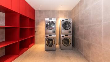A laundry room with two front-loading washing machines, red shelving units, and tiled walls.