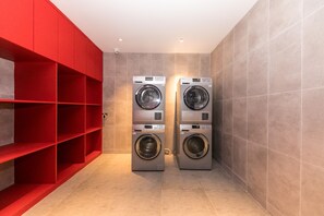 A laundry room with two front-loading washing machines, red shelving units, and tiled walls. - Ibis Hotel (Shanghai)
