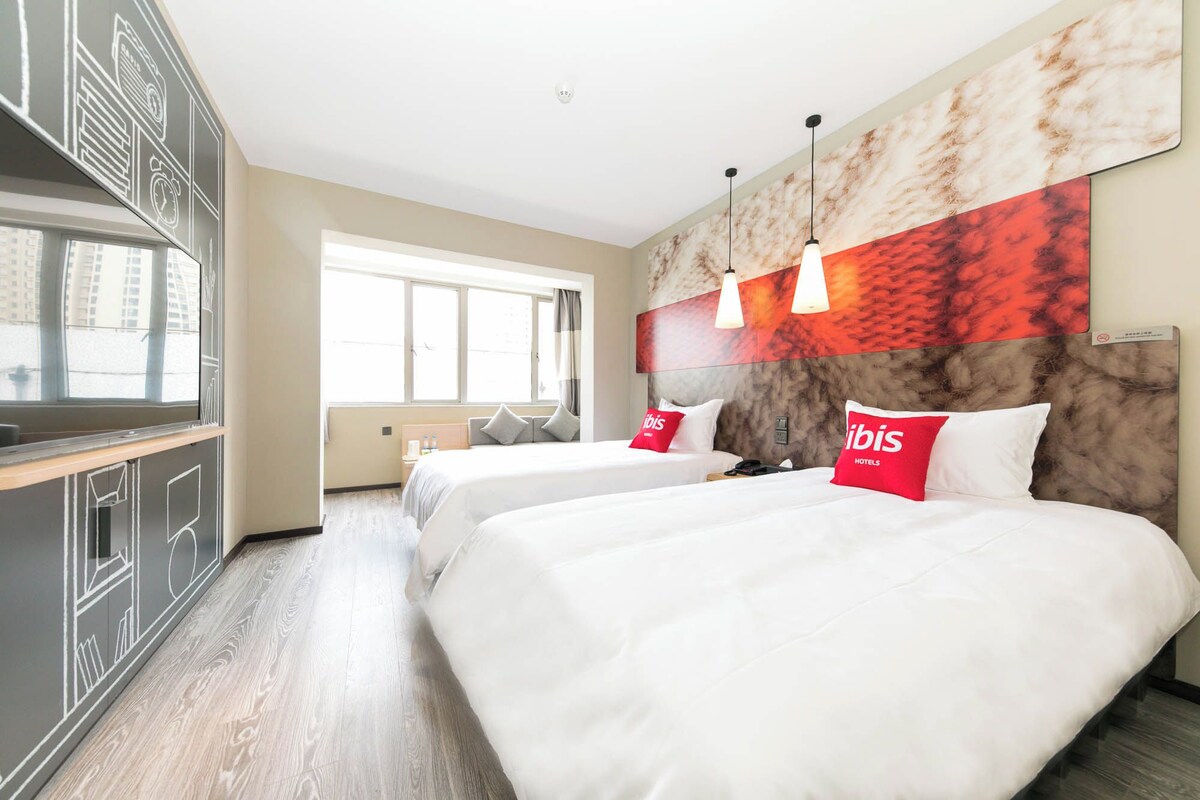 A hotel room with two beds, a large window, and a modern design.