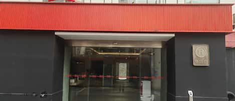 A hotel entrance with a red roof and glass doors, a sign for 'ibis Hotels', and a 'H' logo indicating a hotel.