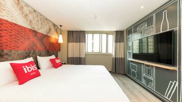 A hotel room with a large bed, two red pillows, a flat-screen TV, and a wall with geometric patterns.