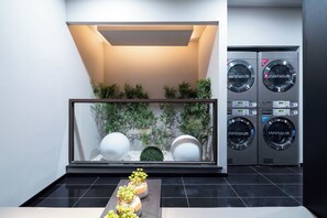 A modern laundry room with two stacked washing machines, a glass display case with decorative items, and a black tiled floor. - Ibis Hotel Tianjin Railway Station Jinwan Plaza (Tianjin)