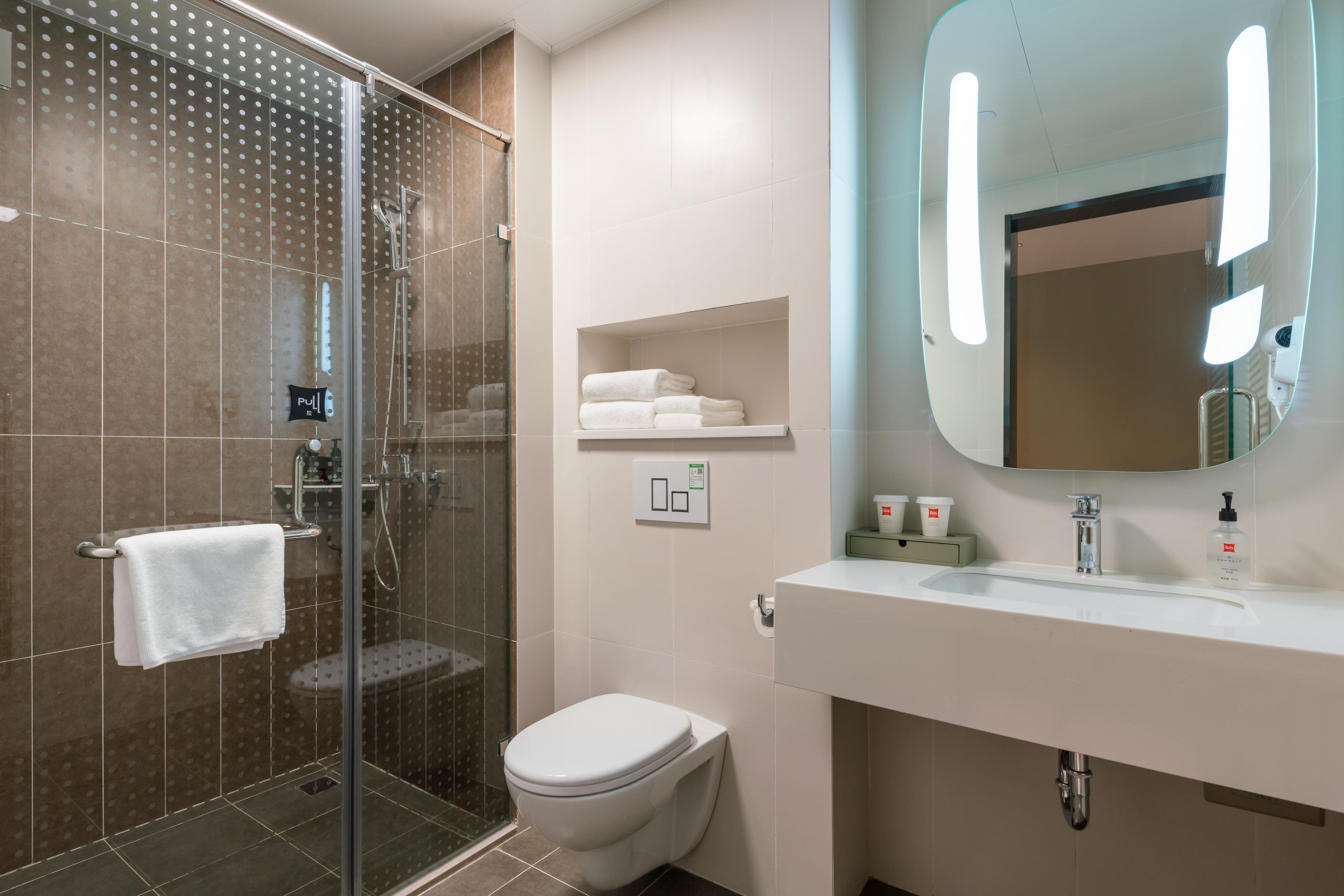 Un baño moderno con cabina de ducha de vidrio, inodoro, lavabo con espejo y un perchero para toallas.